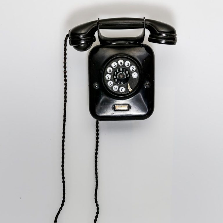Schwarz-weißer Vintage-Telefon mit Drehwähler und Kabel, an einer Wand montiert.