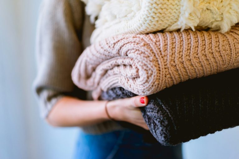 Eine Person hält mehrere gefaltete Pullover in verschiedenen Farben.