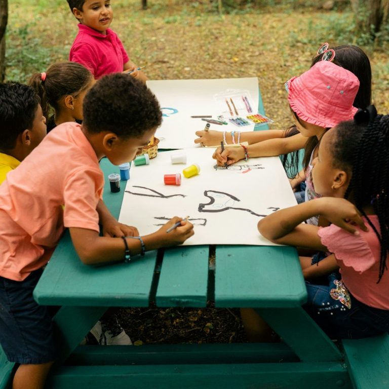 Kinder sitzen an einem Tisch und malen mit bunten Stiften in der Natur.